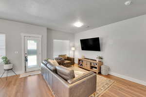 Living room featuring light wood-style floors, a textured ceiling, and baseboards