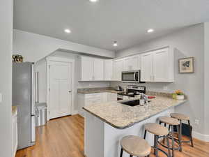 Kitchen featuring appliances with stainless steel finishes, baseboards, a peninsula, a breakfast bar, and light wood-type flooring