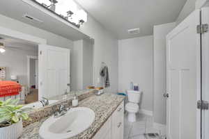 Bathroom featuring baseboards, vanity, toilet, ceiling fan, and marble look tiles