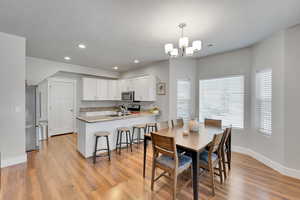 Dining room featuring baseboards, a chandelier, light wood-type flooring, recessed lighting, and a textured ceiling