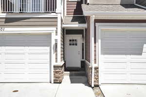 View of exterior entry with stone siding, roof with shingles, a balcony, concrete driveway, and a garage