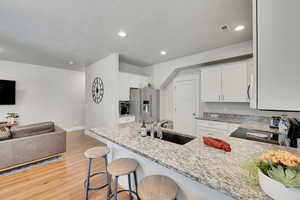 Kitchen featuring black / electric stove, a sink, high end fridge, light wood-style floors, and light stone counters