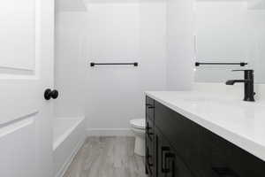 Bathroom with vanity, toilet, wood finished floors, baseboards, and tub / shower combination