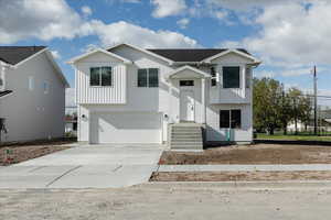 Raised ranch with board and batten siding, an attached garage, and driveway