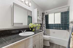 Bathroom featuring vanity, wood finished floors, shower / bathtub combination with curtain, and toilet
