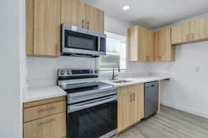 Kitchen featuring stainless steel appliances, light brown cabinetry, a sink, light countertops, and recessed lighting