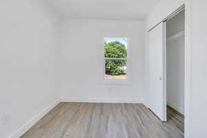 Unfurnished bedroom featuring light wood-style flooring, a closet, and baseboards