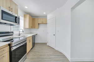 Kitchen featuring stainless steel appliances, light brown cabinetry, a sink, light wood finished floors, and light countertops