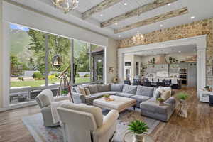 Living room featuring a chandelier, healthy amount of natural light, wood ceiling with exposed beams, a high ceiling, and light wood-style floors