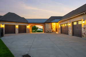 View of front of property featuring a garage, a standing seam roof, driveway, stone siding, and metal roof