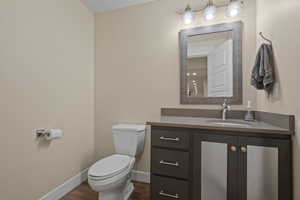 Bathroom featuring toilet, wood finished floors, vanity, and baseboards
