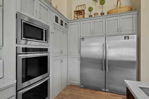 Kitchen featuring built in appliances, light countertops, glass insert cabinets, and light wood finished floors