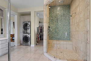 Bathroom featuring stacked washer and clothes dryer, a shower stall, tile patterned floors, baseboards, and a spacious closet