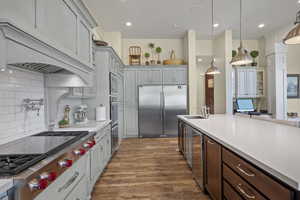 Kitchen with built in appliances, custom exhaust hood, a sink, light wood-type flooring, and light countertops