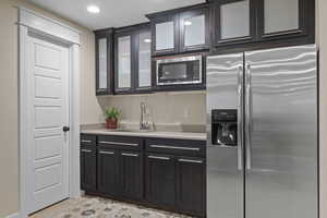 Kitchen featuring appliances with stainless steel finishes, a sink, light countertops, glass insert cabinets, and recessed lighting