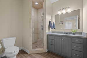 Bathroom with vanity, toilet, wood finished floors, a stall shower, and baseboards