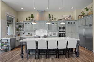 Kitchen featuring built in appliances, light countertops, backsplash, wood finished floors, and recessed lighting