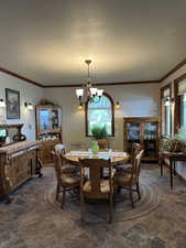 Dining space featuring a chandelier, crown molding, dark stone finish floors, and a textured ceiling