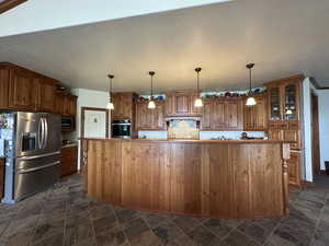 Kitchen with stainless steel appliances, brown cabinets, glass insert cabinets, and dark stone finish floors
