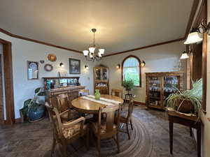Dining room with a chandelier, ornamental molding, baseboards, and dark stone finish flooring