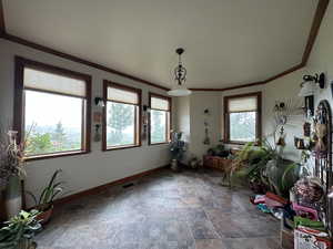 Unfurnished dining area with baseboards, stone finish flooring, and crown molding