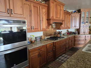 Kitchen with appliances with stainless steel finishes, glass insert cabinets, tasteful backsplash, brown cabinetry, and a textured ceiling