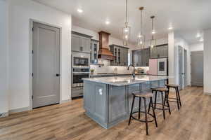 Kitchen with stainless steel appliances, custom exhaust hood, gray cabinets, light wood-type flooring, and recessed lighting
