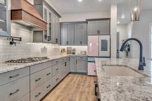Kitchen featuring stainless steel gas stovetop, gray cabinetry, custom exhaust hood, light wood-type flooring, and light stone countertops