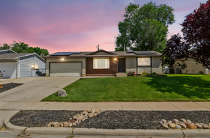 Ranch-style home featuring an attached garage, driveway, a lawn, and roof mounted solar panels