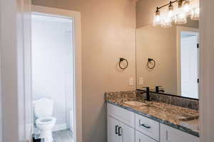 Bathroom featuring vanity, toilet, a chandelier, wood finished floors, and baseboards