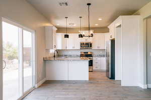 Kitchen featuring stainless steel appliances, a peninsula, a sink, light stone countertops, and light wood-type flooring