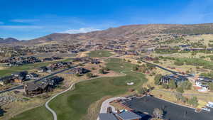 Aerial view of property's location with a golf club, a mountainous background, and nearby suburban area
