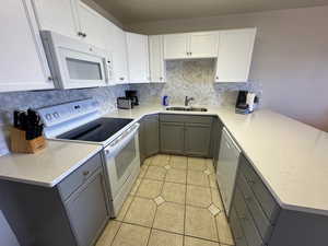 Kitchen featuring white appliances, gray cabinetry, a sink, a peninsula, and tasteful backsplash