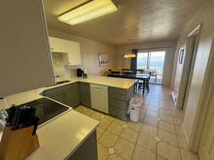 Kitchen with white dishwasher, a peninsula, light countertops, a textured ceiling, and white cabinetry