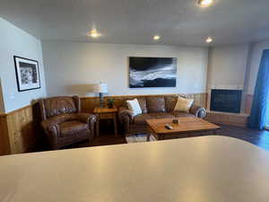 Living room with a wainscoted wall, wood finished floors, a textured ceiling, a tiled fireplace, and recessed lighting
