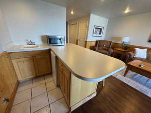 Kitchen with a sink, stainless steel microwave, dishwashing machine, a wainscoted wall, and a textured ceiling