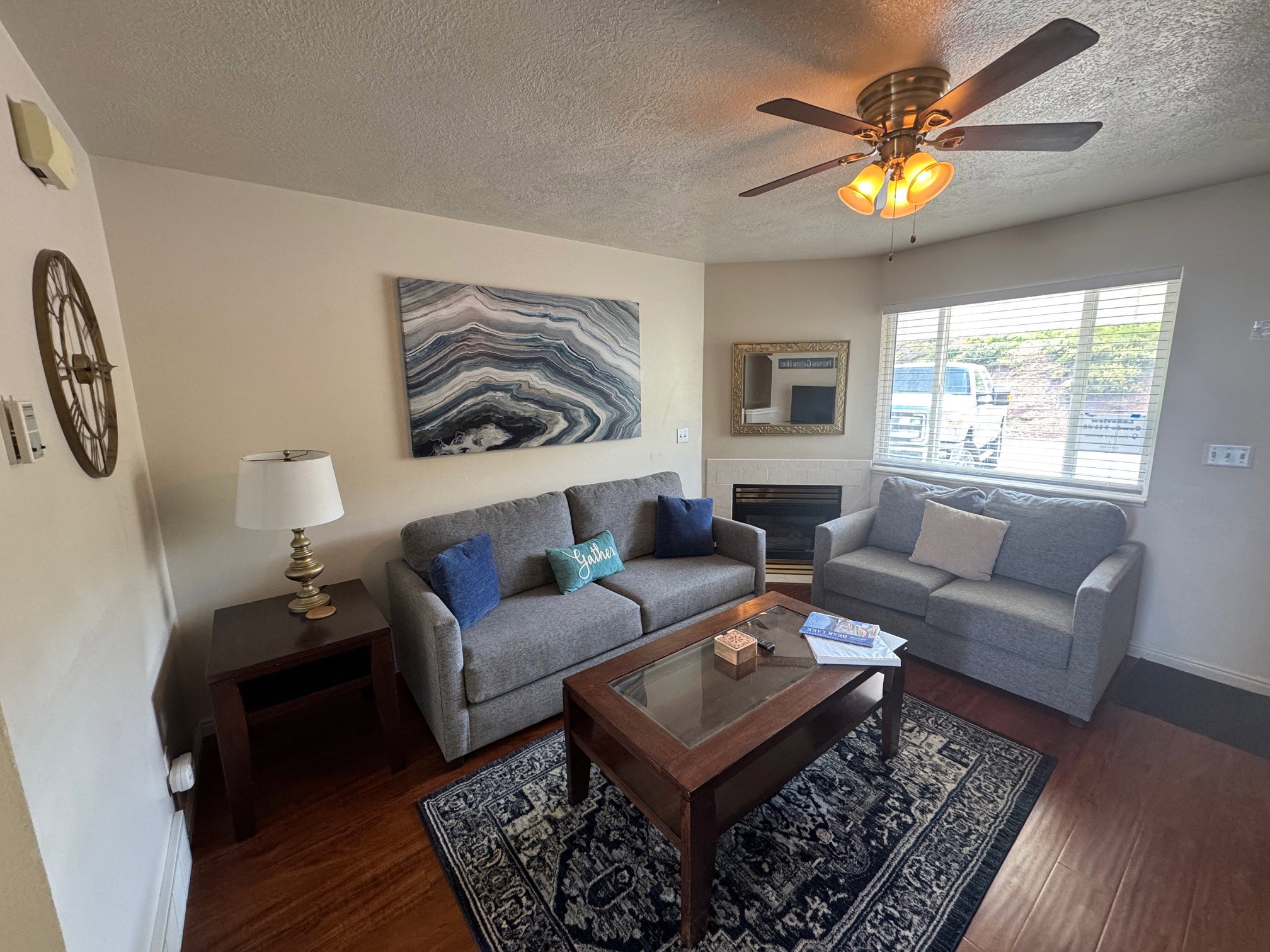 Living area featuring a textured ceiling, wood finished floors, ceiling fan, baseboards, and a tile fireplace