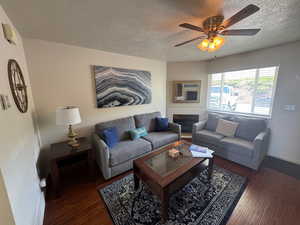 Living area featuring a textured ceiling, wood finished floors, ceiling fan, baseboards, and a tile fireplace