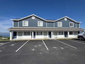 Townhome / multi-family property featuring uncovered parking, covered porch, and a shingled roof