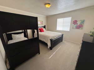 Bedroom featuring a textured ceiling, ornamental molding, light colored carpet, and baseboards