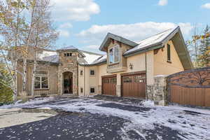 View of front facade with stone siding, driveway, stucco siding, and a gate