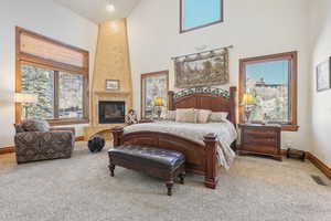 Carpeted bedroom with a towering ceiling, baseboards, multiple windows, and a premium fireplace