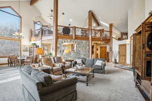 Carpeted living room featuring high vaulted ceiling, beam ceiling, ceiling fan, a chandelier, and baseboards