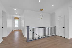 Hallway with wood finished floors, baseboards, recessed lighting, and an upstairs landing
