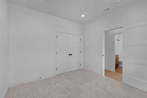 Unfurnished bedroom featuring light carpet, baseboards, recessed lighting, a closet, and ensuite bathroom