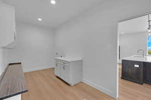 Laundry area featuring a sink, baseboards, light wood-style flooring, and recessed lighting
