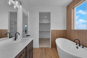 Full bathroom with vanity, a soaking tub, a spacious closet, wood finished floors, and wainscoting