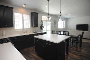 Kitchen with a sink, dark cabinets, dark wood-style floors, tasteful backsplash, and light countertops