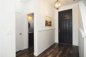 Foyer featuring dark wood-type flooring, a chandelier, and wainscoting