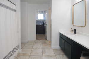 Full bath featuring vanity, baseboards, and marble look tiles